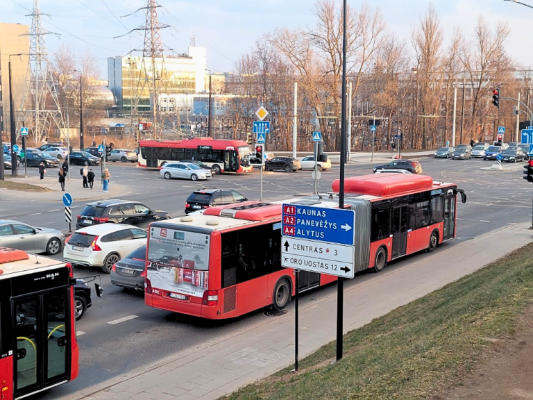 Two red buses standing one behind the other at an intersection, with a red and white trolleybus waiting to turn left and several cars nearby.