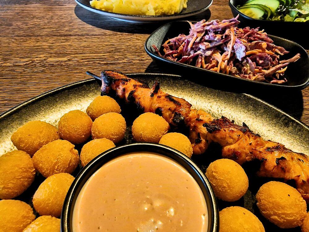 Grilled chicken skewers at Grill London in Vilnius served with golden fried potato balls and creamy dipping sauce and red cabbage slaw and salad on a wooden table.