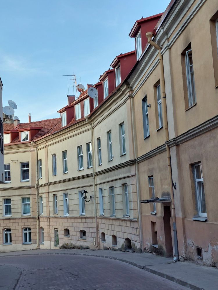 A quiet curved street in Vilnius Old Town lined with pale historic buildings, red roofs, windows and satellite dishes.