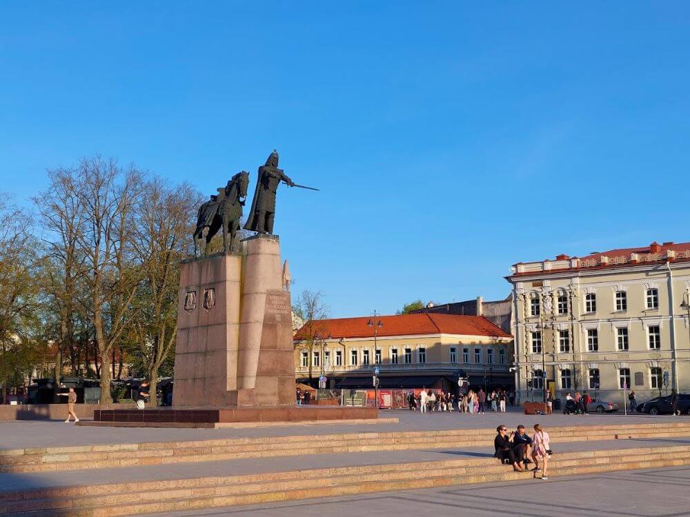 The Gediminas monument in Cathedral Square in Vilnius with broad stone steps, historic buildings, and a clear blue sky.
